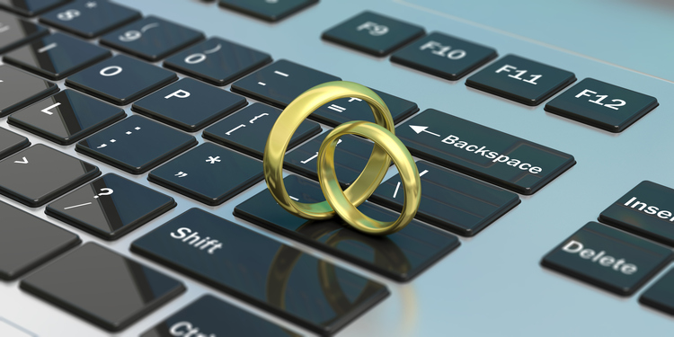 Two gold wedding rings rest on the keys of a computer keyboard. The rings are positioned near the backspace key, symbolizing the concept of ending a marriage.