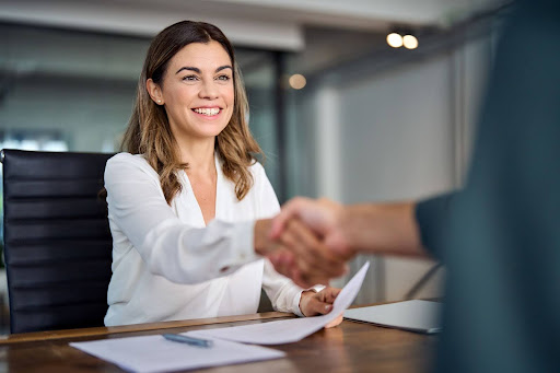 Smiling woman in a white blouse shaking hands across a desk, holding papers in a bright office setting.
. what to bring to a child custody consultation