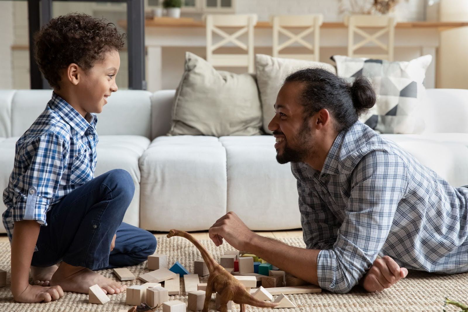 Father and son smiling while playing with wooden blocks and toy dinosaurs on living room floor. collin county family law attorney.